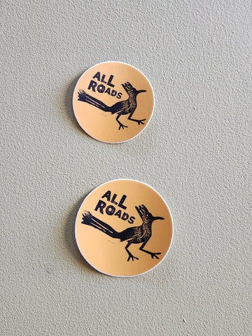 Two round stickers with a roadrunner graphic and 'All Roads' text on a gray background.
