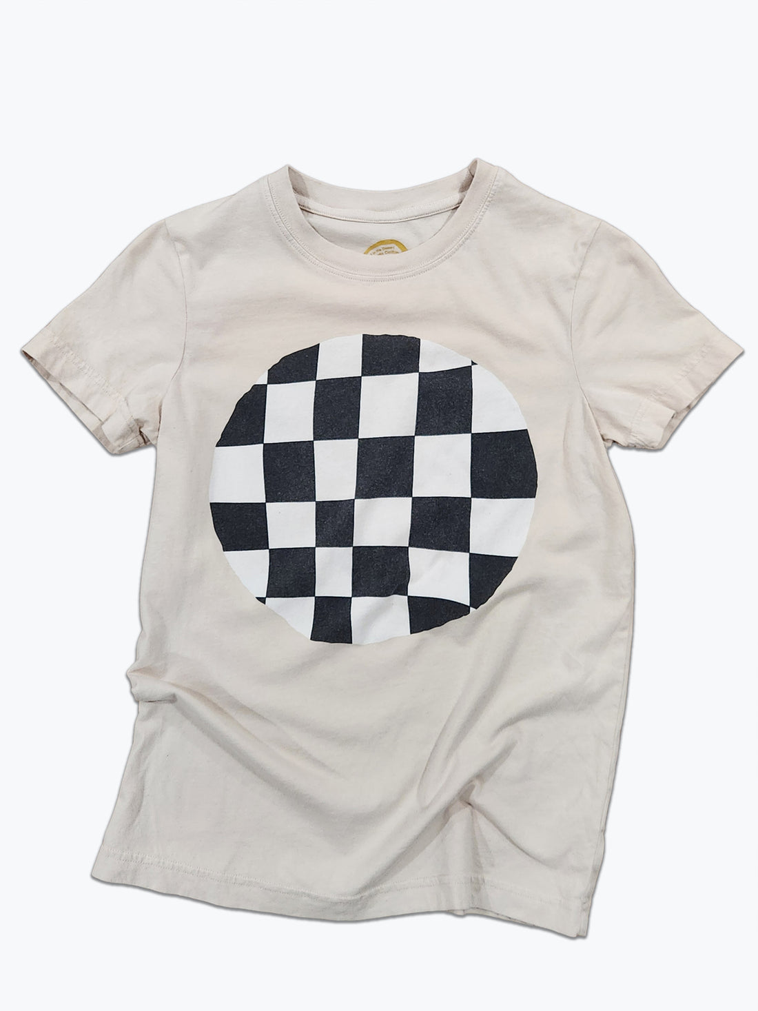 A light beige crewneck t-shirt featuring a large circular black and white checkerboard graphic printed on the chest, displayed flat against a white background.