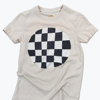 A light beige crewneck t-shirt featuring a large circular black and white checkerboard graphic printed on the chest, displayed flat against a white background.