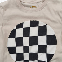 A close-up of a beige crewneck t-shirt featuring a large circular black and white checkerboard graphic printed on the front.