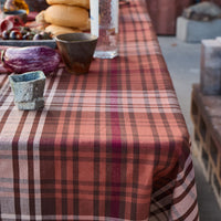 Table with a plaid tablecloth, various items including bread and bottles, on an outdoor setting.
