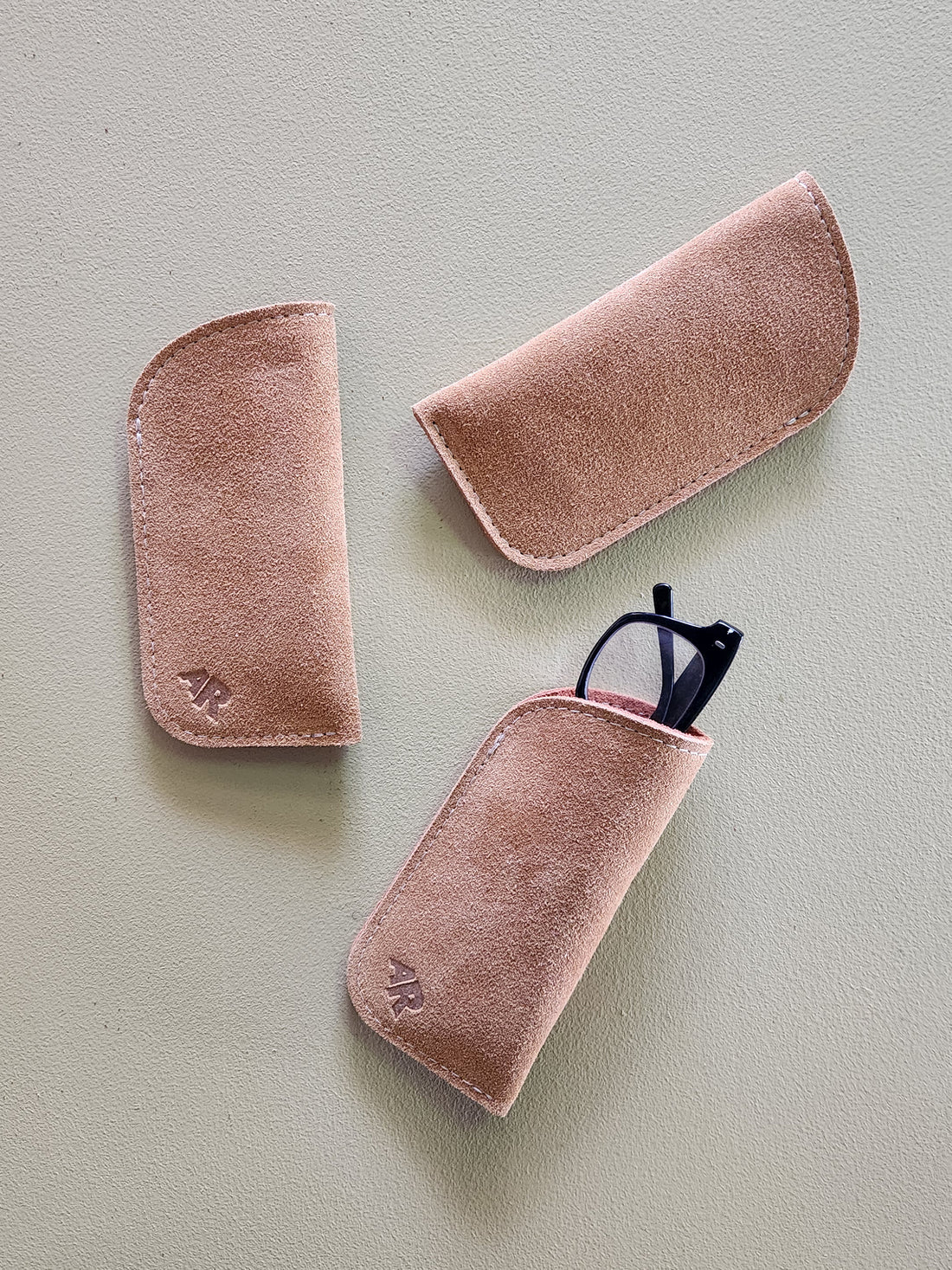 Three tan suede eyeglass cases on a light gray background