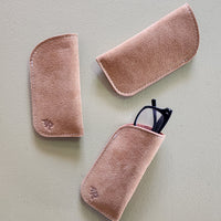 Three tan suede eyeglass cases on a light gray background