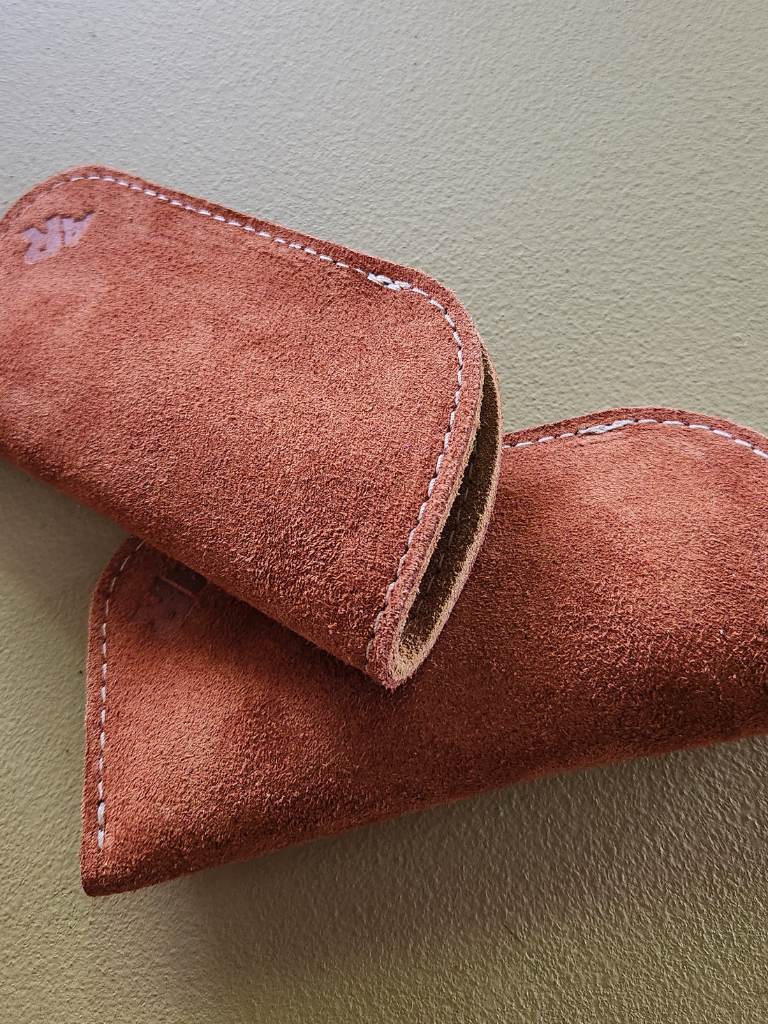 Close-up of a brown suede eyeglass case on a light green background