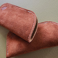 Close-up of a brown suede eyeglass case on a light green background