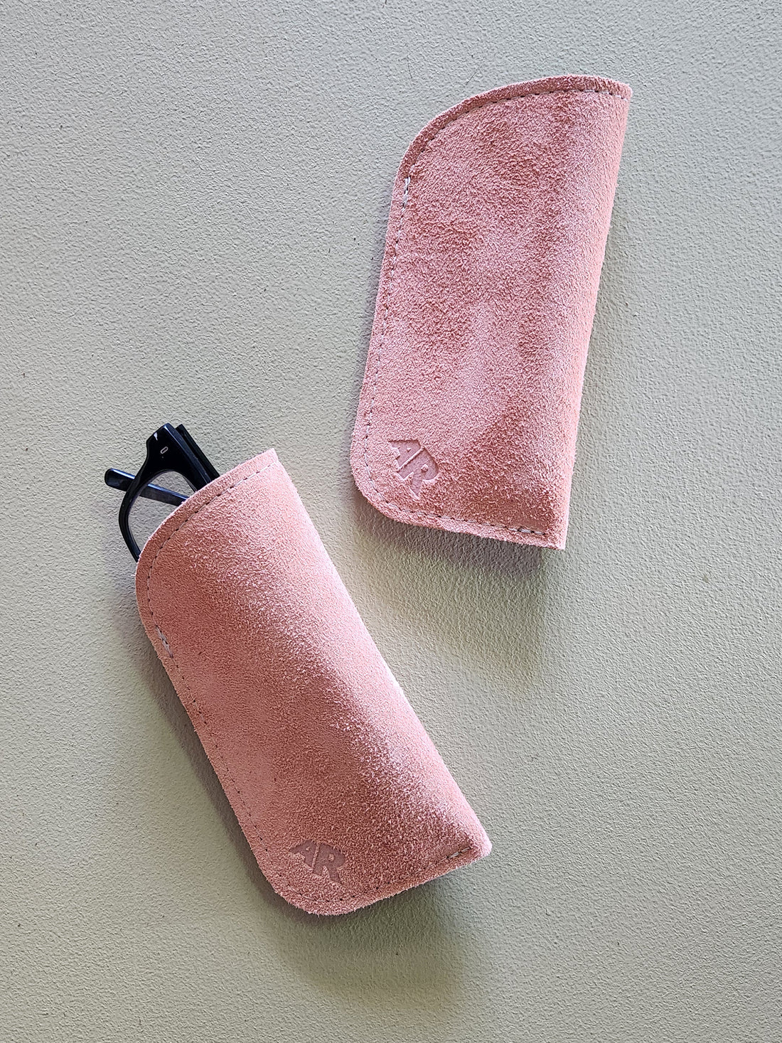 Two tan suede eyeglass cases on a light gray background