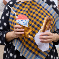 A person holding two checkered napkins in navy, ochre, and slate blue colors.