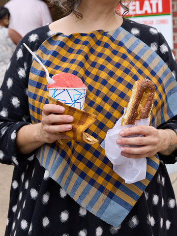 A person holding two checkered napkins in navy, ochre, and slate blue colors.