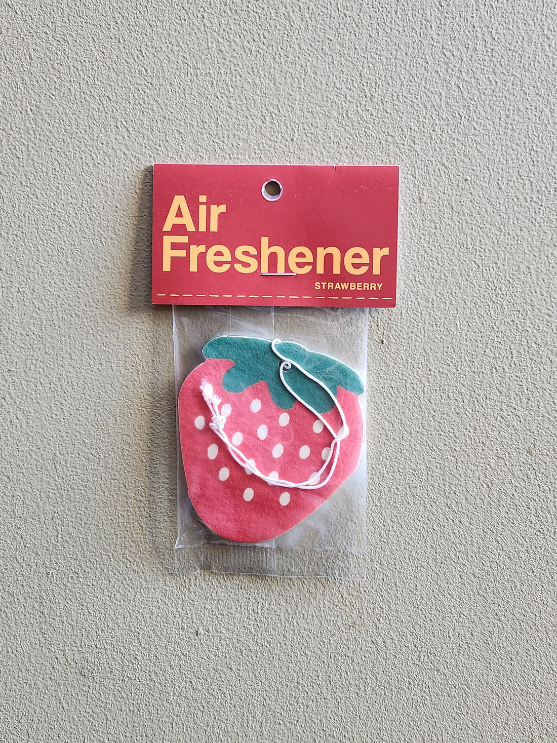 A strawberry-shaped air freshener in a clear plastic bag with a red header card that reads &