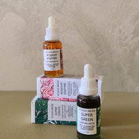 Two bottles of facial oils with their packaging on a neutral background