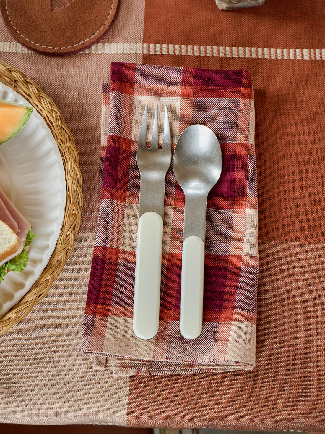 Silver fork and spoon on a purple and white checkered napkin with a plaid tablecloth.