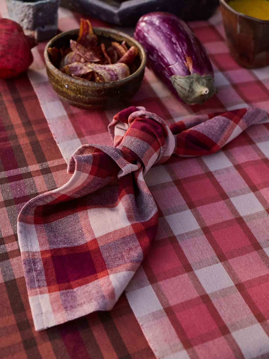 Plaid napkin on a checkered tablecloth with vegetables and a bowl.