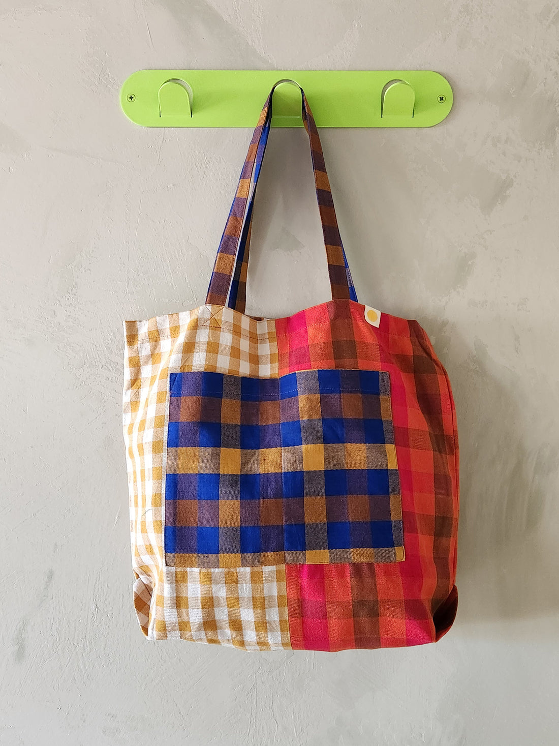 Colorful plaid bag hanging on a green hook against a light gray background