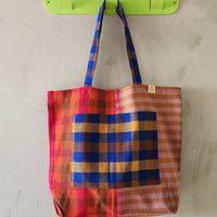 Colorful checkered tote bag hanging on a green hook against a light gray wall.
