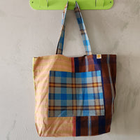 Colorful plaid tote bag hanging on a green hook against a beige wall.