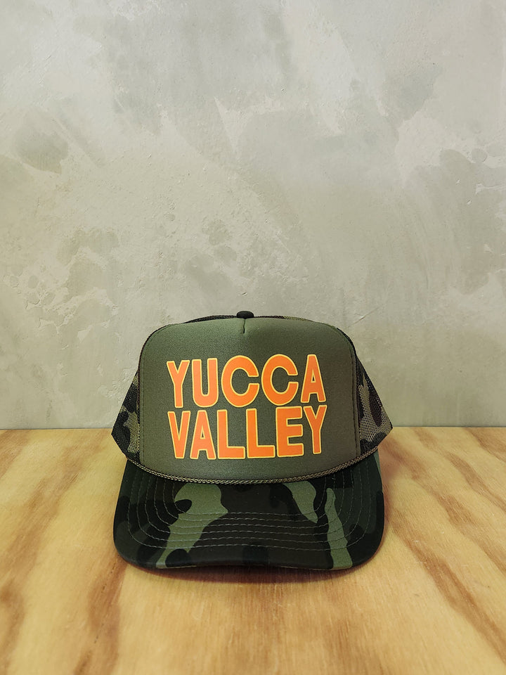 Army green camo foam trucker hat with the text Yucca Valley.