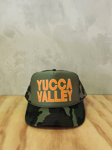 Army green camo foam trucker hat with the text Yucca Valley.